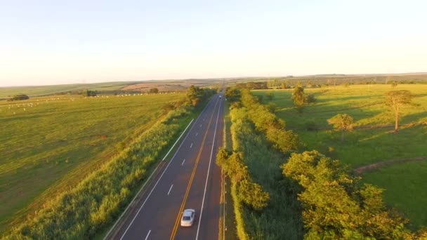 Дорога на заході сонця з прохідним автомобілем і красивим пасовищем на задньому плані — стокове відео