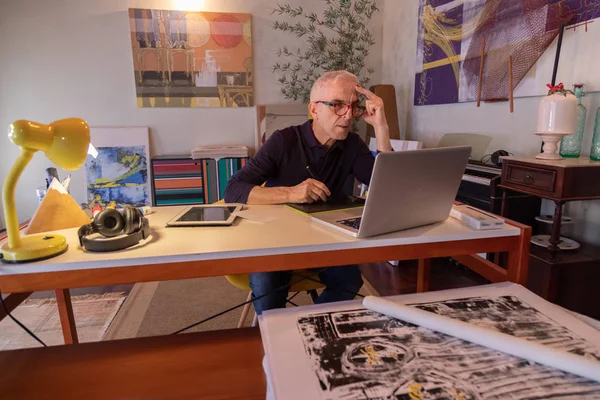Middle aged man using computer in his art studio and drawing on his tablet
