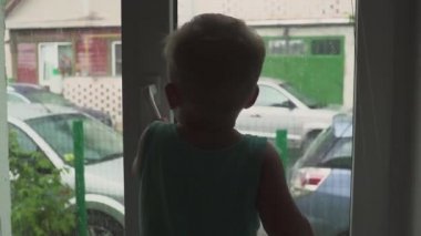 Bir çocuk bir pencere standları ve sokakta yağmur yağacak. Yağmur oynatımını durdurur