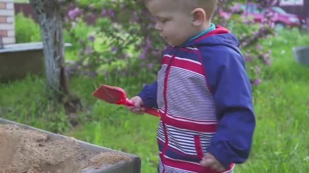 Mały chłopiec gra z piaskownicy i chusteczki piasek z trampki. — Wideo stockowe