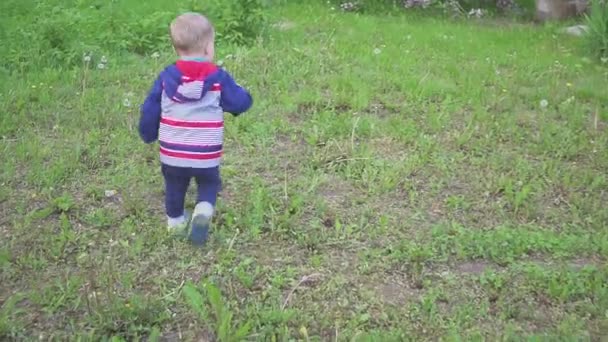 Ein kleiner Junge spielt mit einem Sandkasten und wischt Sand von den Turnschuhen. — Stockvideo