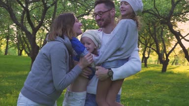 Mutlu aile çimlere sarılma. Anne ve iki kızı park çimenlikte kucaklayan. Çiçekli meyve bahçesi.