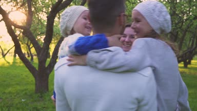 Mutlu aile çimlere sarılma. Anne ve iki kızı park çimenlikte kucaklayan. Çiçekli meyve bahçesi.