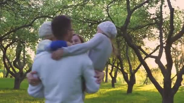 快乐的家庭拥抱在草地上。父母和他们的两个女儿正在公园的草坪上拥抱。开花果园. — 图库视频影像