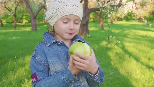 Petite fille portrait manger pomme verte en plein air. Une fille avec une pomme sur le fond des jardins fleuris .