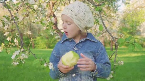 Niña comiendo manzana verde en los jardines de flores . — Vídeo de stock
