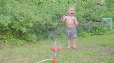 Sevimli küçük çocuk dışında su fıskiye yaz bahçede eğleniyor. Ağır çekim