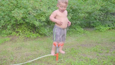 Mutlu küçük çocuk dışında su fıskiye yaz bahçede eğleniyor. Ağır çekim