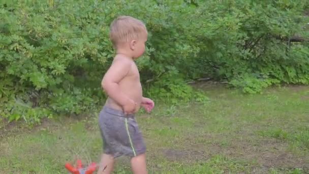 Lindo niño divirtiéndose al aire libre con aspersor de agua en el jardín de verano. Movimiento lento — Vídeo de stock