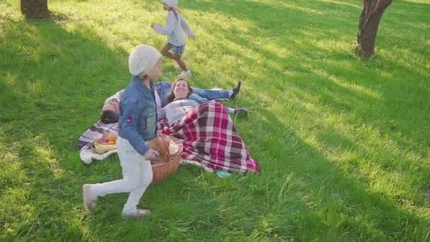 Föräldrar liggande på gräset, har deras två döttrar roligt och rinnande bakgrund i park. Familjesemester i landskapet. — Stockvideo