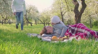 Mutlu aile piknik çiçek açması elma ağacının yakınında saat harcıyor. Anne çim, çocuk ve kocası onunla çalıştırmak yatıyor. Herkes anne kisses.