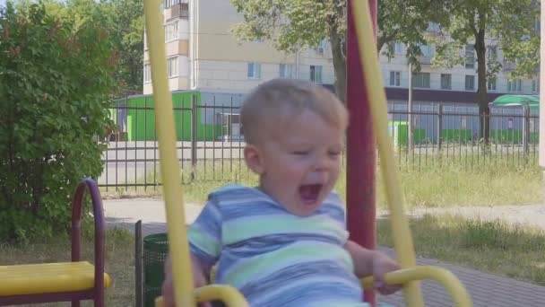 Porträt eines zweijährigen Jungen, der im Hintergrund der Stadt auf einer Schaukel reitet. Zeitlupe — Stockvideo