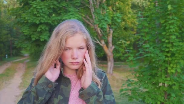 Detailní portrét docela dospívající smutná dívka při pohledu na fotoaparát. Bílý usmívající se šťastně s přírodní blond dlouhé vlasy stojící venku. — Stock video