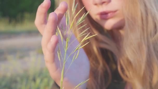 Retrato de la joven rubia de 11 años. Pensativa y soñadoramente mira la hoja de hierba . — Vídeo de stock