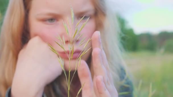 Retrato de la joven rubia de 11 años. Pensativa y soñadoramente mira la hoja de hierba . — Vídeo de stock