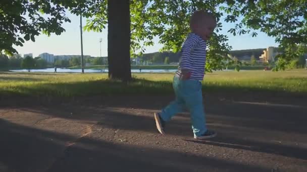 joyeux petit garçon courant le long du trottoir sur le fond du parc et du lac et souriant au ralenti 