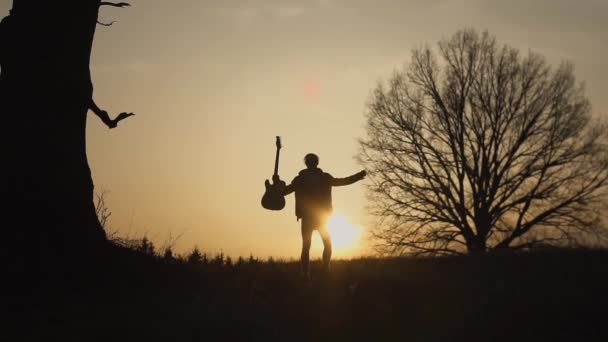 Sylwetka gitarzysty o zachodzie słońca zwolnionym tempie. Gitarzysta fale rękę — Wideo stockowe