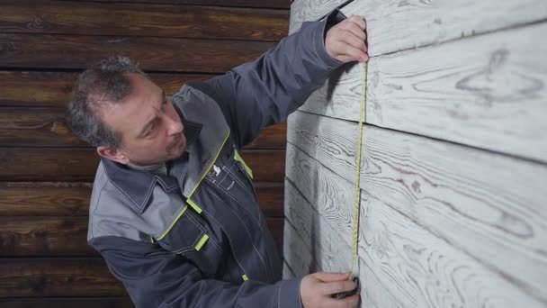 Pracownik mierzy drewnianą ścianę z linijką — Wideo stockowe