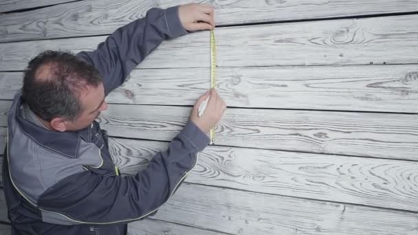 The worker measures a wooden wall with a ruler — Stock Video