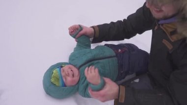 Baba ve oğul. Küçük bir çocuk kar üzerinde yatıyor ve baba öper ve onu gıdıklıyor. mutlu bir aile. Herkes gülümsüyor.