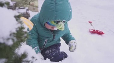 çocuk çocuk Noel ağacı yakınındaki kar üzerinde yatıyor ve açık süslemeleri ile oynanır.
