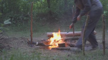 Kazan üzerinde akşam ormanda kamp ateşi ile makarna pişirme. Aşçı yemek bir kaşıkla kıpırdanırken..