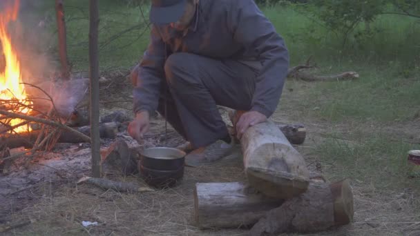 Viandante maschio mangia dal piatto vicino al fuoco in serata — Video Stock