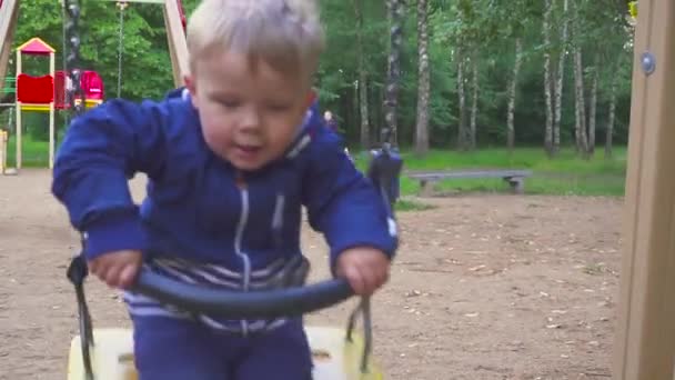 Двухлетний мальчик катается на качелях в парке — стоковое видео