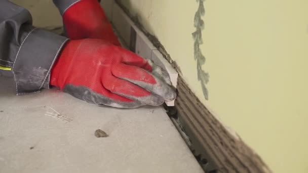 Trabalhador define pequenas telhas na parede na cozinha. As mãos dele estão a colocar a telha no adesivo. tiroteio stedikam. close-up — Vídeo de Stock