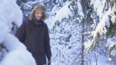 Kar kış orman seyahat sırt çantası ile yürüyen adam. kameraya elini sallayarak