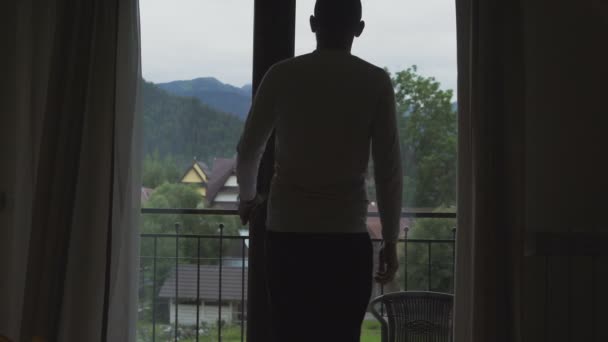 Mladý člověk jde z jeho pokoje na balkón, podívejte na hory. — Stock video