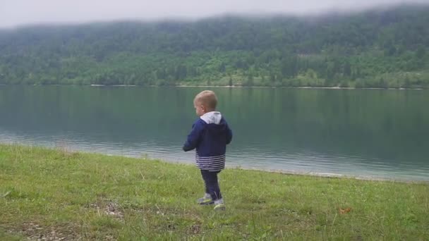 El niño camina cerca del lago de la montaña. Correr y retozar en la naturaleza. Movimiento lento — Vídeo de stock