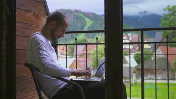 Freelancer man met een computer in een bergdorp, tegen een achtergrond van een berglandschap — Stockvideo