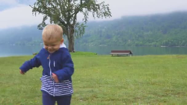 A kisfiú jár, a hegyi tó közelében. Futás és ficánkolódnak a természetben. — Stock videók
