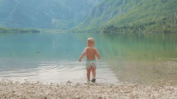 Ragazzino 2 anni nell'acqua del lago di montagna foresta. Vista dal retro . — Video Stock