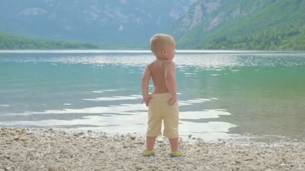 Niño pequeño 2 años en el agua del bosque lago de montaña. Vista desde atrás . — Vídeos de Stock