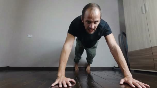 El tipo empujó del suelo con una cara cansada y tensa. hombre joven entrena en casa . — Vídeo de stock