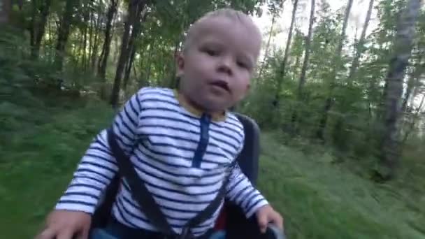 Criança menino sentado na cadeira de bicicleta enquanto dirige e olhando ao redor — Vídeo de Stock