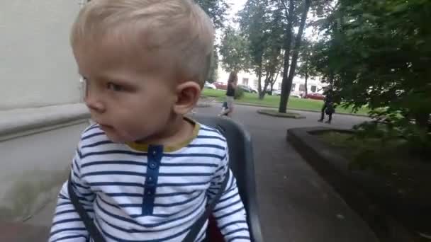 Kind jongen op fiets stoel zitten terwijl rijden en rondkijken — Stockvideo