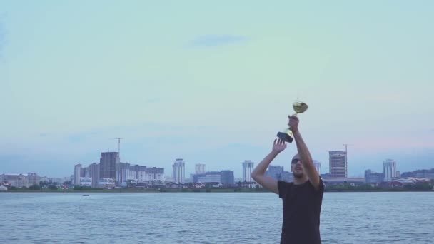 Um jovem com um copo nas mãos se alegra com a vitória esportiva. Danças e saltos na cidade da noite. Conceito como vitória, sucesso e campeão no esporte. Movimento lento — Vídeo de Stock