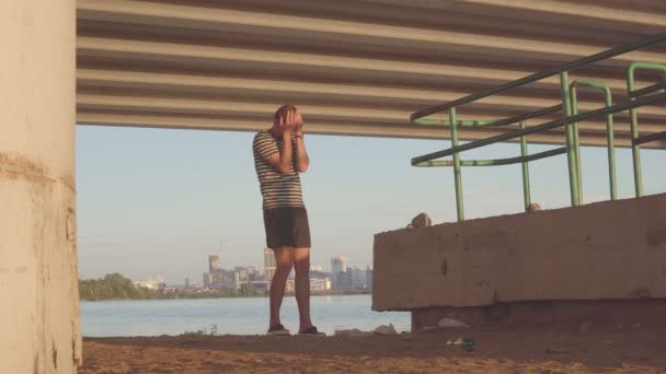 Jovem depressivo sob a ponte, contra o pano de fundo da cidade da noite — Vídeo de Stock