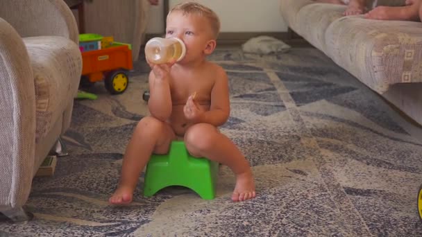 Lindo chico sentado en una olla en casa, viendo dibujos animados en la televisión. comer y beber . — Vídeos de Stock