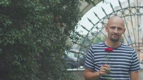 Hombre está esperando a que su chica se reúna con una rosa y agitando su mano. feliz reunión — Vídeos de Stock