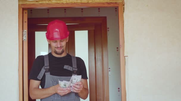 The worker in a construction with helmet counts money dollars against the background of the repaired apartment — Stock Video