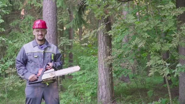 Portret van de werknemer in een helm met een kettingzaag in het bos — Stockvideo