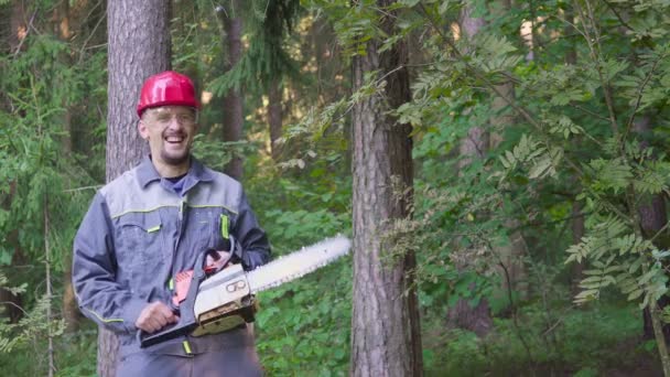 Портрет смеющегося рабочего в шлеме с бензопилой в лесу — стоковое видео