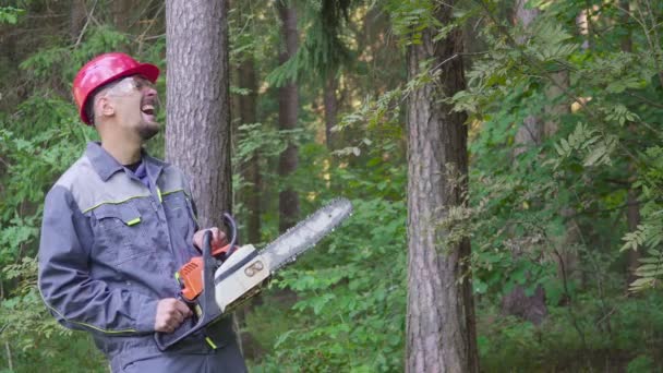 Porträt eines lachenden Arbeiters mit Helm und Kettensäge im Wald — Stockvideo