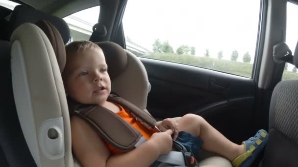 Lille dreng i børnenes autostol i bilen. Knægten smiler, griner og vinker lykkeligt med hænderne . – Stock-video