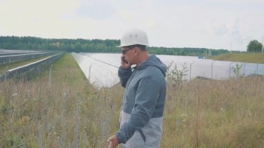 Bir güneş güç istasyonu ve jestleri yakınındaki telefonda konuşan işçi portresi.