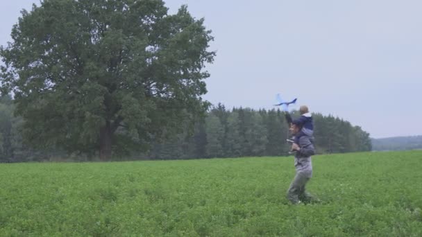 Una familia feliz. El chico de su padre jugando con un juguete de avión en el campo — Vídeos de Stock